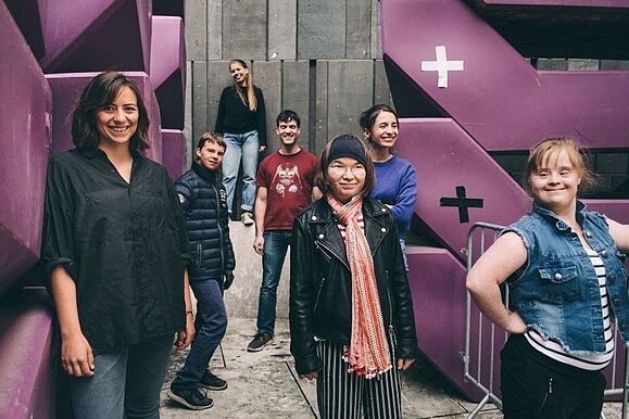 Die Redaktion andererseits bringt jungen Wind in den österreichischen Diskurs um Behinderung. Foto: Stefan Fürthbauer. mehrere Menschen stehen vor lila Platten und lächeln in die Kamera