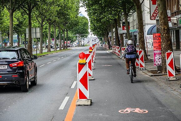 Pop-up-Radweg auf der Lassallestraße, Copyright: Stadt Wien Eine dreispurige Straße ist geteilt durch Trennelemente. 2 Spuren sind für Autofahrer, 1 Spur ist für Radfahrer.