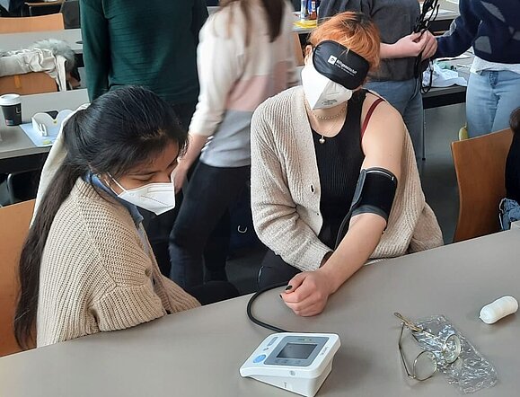 junge Frau misst Blutdruck einer anderen jungen Frau mit Augenbinde