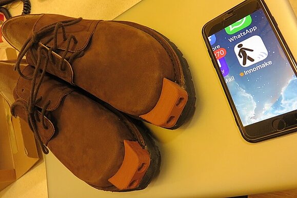 Braune Schuhe der Marke „Waldviertler“ mit eingebauten Sensoren Braune Herrenschnürrschuhe mit Applikation vorne, daneben ein Smartphone mit der App Innomake.