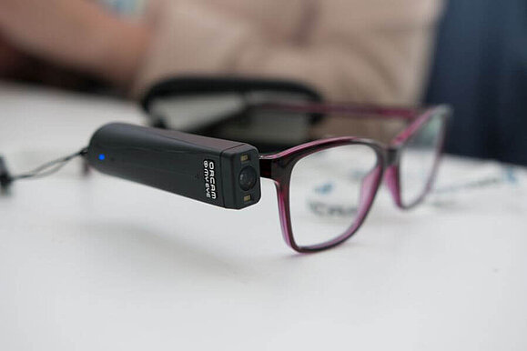 Rote Brille, am rechten Bügel OrCam Gerät befestigt.