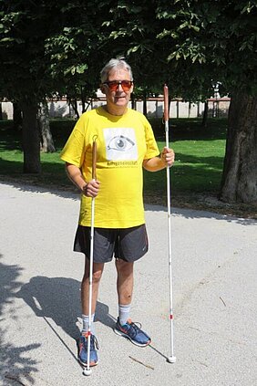 Die zusätzliche Länge des Langstockes ist ideal für Hobbyläufer. In seiner rechten Hand hält Harald einen Langstock der bis zu den Achseln reicht, in seiner linken Hand einen Langstock der bis zum Kinn reicht.