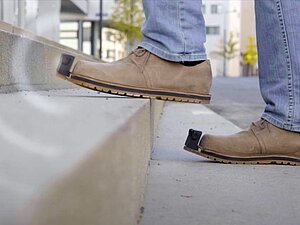 InnoMake_StufenAufwärts_Wellen_©Tec-Innovation Person mit braunen InnoMake-Schuhen geht Stufen aufwärts. InnoMake-Sensor sendet Wellen aus.