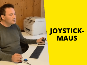 Eine Joystickmaus wird von Menschen mit erschwerter Motorik gern am Arbeitsplatz genutzt. Mann sitzt am Schreibtisch und bedient einen Joystick und zwei Knöpfe, rechts Text auf gelb "Joystick Maus"