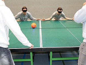 Copyright Christian Sukdolak Zwei Menschen mit Augenbinden stehen hinter zwei zusammengeschobenen Tischtennistischen. Sie beugen sich mit ausgebreiteten Armen zum Tisch hinunter, um zu verhindern, dass ein Ball vom Tisch rollt.