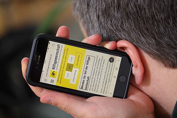 In der APA werden die Weichen für digitale Barrierefreiheit gesetzt. Mann hält sich Smartphone zum Hören ans Ohr