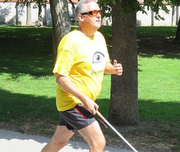 Ein zu kurzer Langstock beim Laufen verursacht eine asymmetrische Haltung und stört den Lauffluss. Harald läuft mit einem Langstock nach EU-Norm in einem Park.