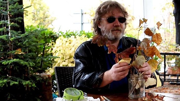 Der Maler Sergej Popolsin bei der Arbeit, Copyright: Sergej Popolsin Sergej Popolsin tastet getrocknete Herbstblätter in einer Vase ab.