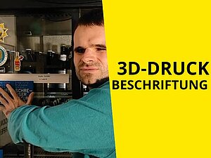 Mann greift hinter sich an 3D Schild, das an einem Kühlschrank klebt. Text: "3D-Druck Beschriftung"