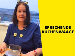 Frau mit Blindenanstecker sitzt an Tisch, vor ihr eine Küchenwaage.
